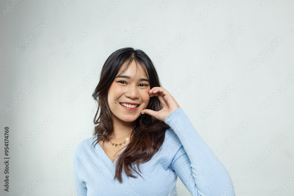 Beautiful young Asian woman with tan skin, toothy style smile with hand on her cheek, face and skin care concept, smooth blue top, white studio background Beautiful young Asian woman with tan skin, toothy style smile with hand on her cheek, face and skin care concept, smooth blue top, white studio background
