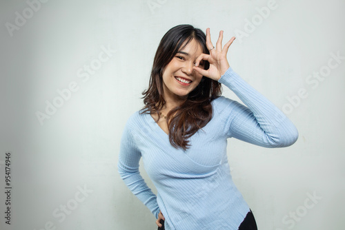 beautiful asian girl smooth long hair in blue top casual suit with ok hand gesture in her curly eyes isolated on white background, blushing face asian woman