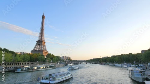 Eiffel Tower and Seine River at Dusk with Boats Passing By. Evening view of the Eiffel Tower by the Seine River in Paris, with boats cruising under a clear sky

