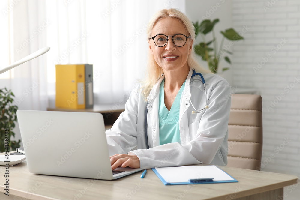 Mature female doctor working with laptop at table in clinic Mature female doctor working with laptop at table in clinic