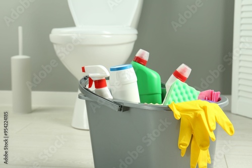 Bucket with different toilet cleaners, rag, sponge and gloves in bathroom