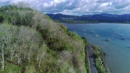 Aerial view of a scenic road near Sekotong, Lombok, Indonesia, featuring lush greenery, a winding road, and a dramatic cliff face. photo