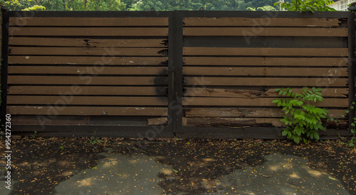 An old weathered wooden garage  entrance gate with fallen rotting leaves in the foreground.  