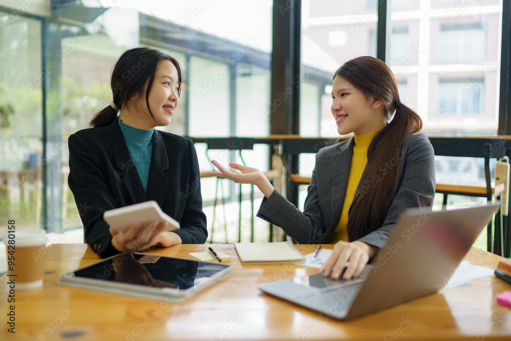 Two young Asian businesswomen discussed investment project work and planning strategy. Business people talk together on laptop computers at the office. Two young Asian businesswomen discussed investment project work and planning strategy. Business people talk together on laptop computers at the office.