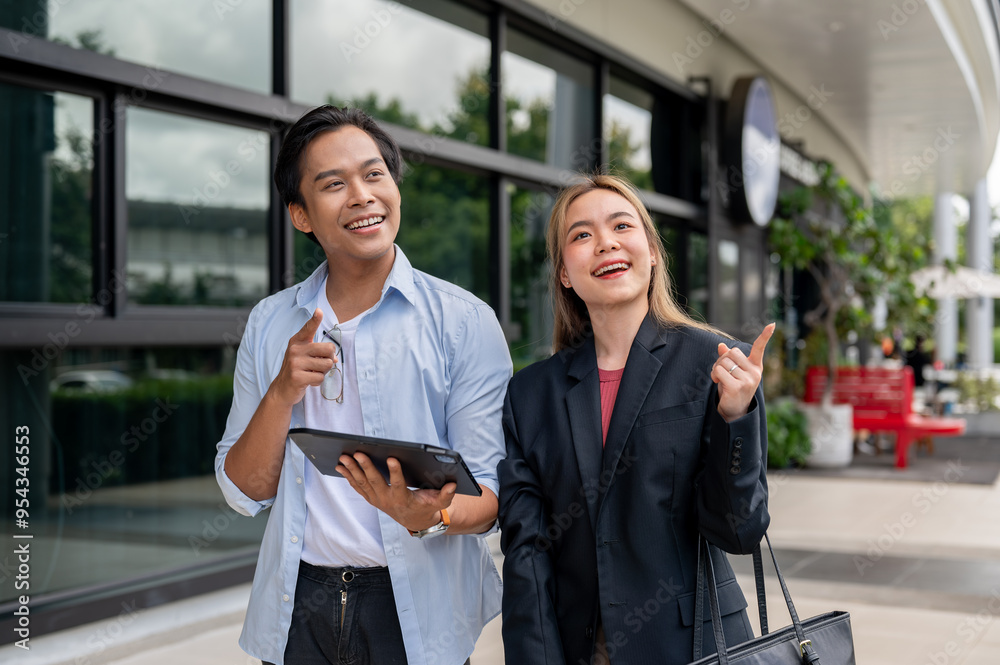 Two cheerful Asian businesspeople are walking outside along a building. Two cheerful Asian businesspeople are walking outside along a building.