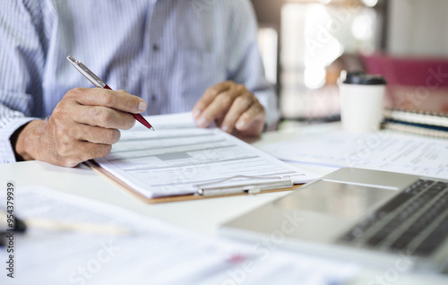 Asian businessman or lawyer working on desk with laptop holding pen checking business contract and document report before sign, Close-up shot photo