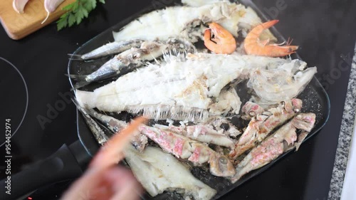 Preparation of delicious seafood meal. Variety of shrimp, red mullet, sardines and sole fish, sizzling in hot pan on stovetop. High quality 4k footage photo