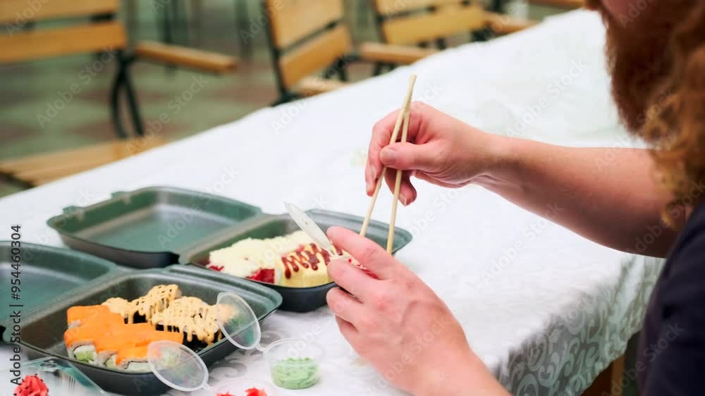 Side view of hungry redhaired young man eating delicious Japanese rolls dipping them in soy sauce holding them in chopsticks. Side view of hungry redhaired young man eating delicious Japanese rolls dipping them in soy sauce holding them in chopsticks.