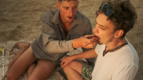 Picnic on the beach young LGBT male couple in love hugging and kissing on sitting on the sand. Top view.