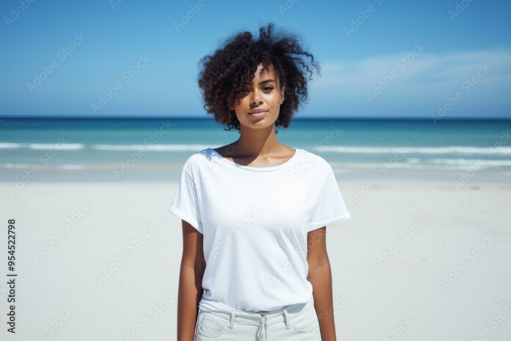 A woman with curly hair stands on a beach wearing a white shirt and jeans A woman with curly hair stands on a beach wearing a white shirt and jeans