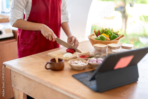 Woman following online cooking course cutting vegetables on wooden board photo