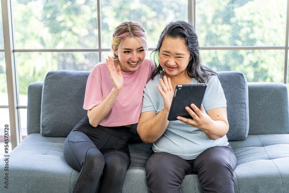 Obraz premium Happy senior asian mother and young daughter waving hands looking at web camera using tablet for video call, smiling mom and girl having fun greeting online by computer webcam making videocall