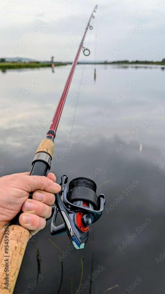 Hand holding fishing rod and reel, fishing at Corrib river at Galway, Ireland, spinning, angling, catch and release, sport and leisure, nature background