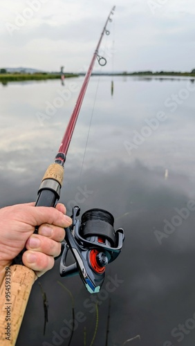 Obraz na płótnie Hand holding fishing rod and reel, fishing at Corrib river at Galway, Ireland, spinning, angling, catch and release, sport and leisure, nature background w salonie