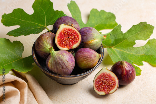 Bowl with fresh ripe purple figs fruit with green leaves. Beige table surface.