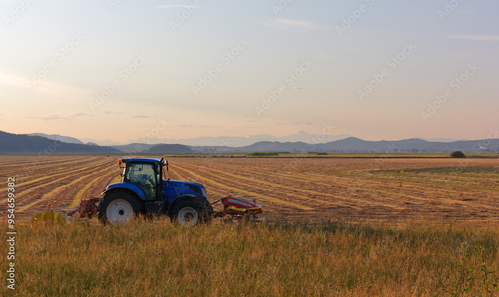Blue tractor at the edge of an agricultural field at sunset Blue tractor at the edge of an agricultural field at sunset