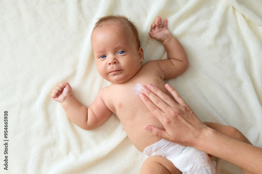 Unknown woman massaging belly of newborn baby on bed for stomach pain relief mother taking care of daughter or son health on white sheet at home Unknown woman massaging belly of newborn baby on bed for stomach pain relief mother taking care of daughter or son health on white sheet at home