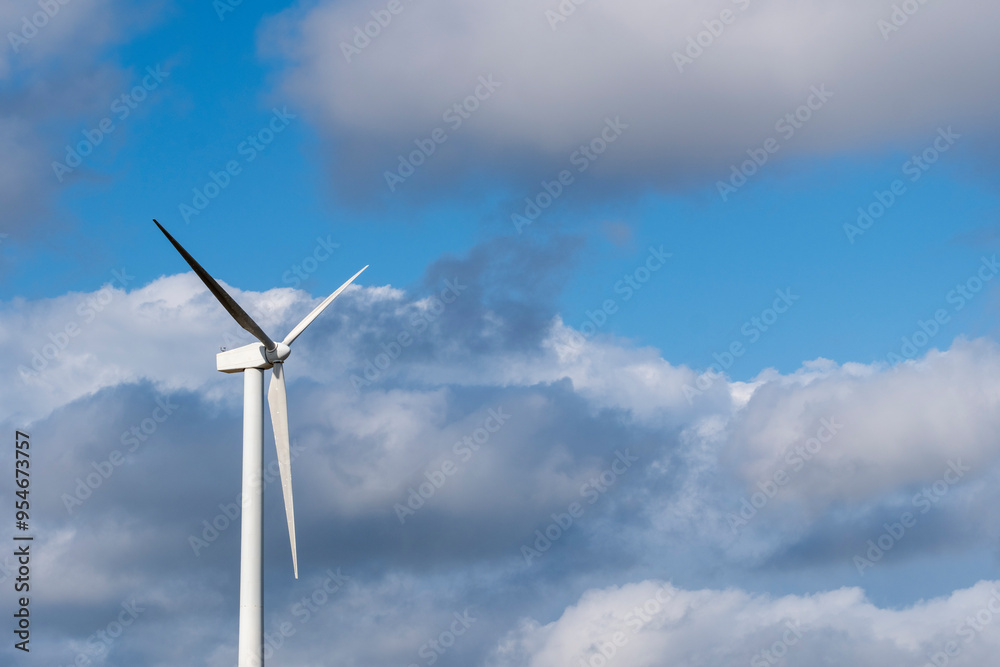 A lone wind turbine stands tall against a backdrop of clouds in a blue sky, symbolizing the solitary strength and commitment to renewable energy and a sustainable future in Tarragona Spain A lone wind turbine stands tall against a backdrop of clouds in a blue sky, symbolizing the solitary strength and commitment to renewable energy and a sustainable future in Tarragona Spain
