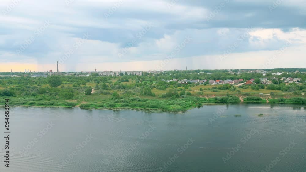 Aerial view of Daugavpils, a Latvian city, showcasing the riverbank, expansive greenery, and urban skyline with a prominent factory pipe under a cloudy sky. Location: Daugavpils, Latvia Aerial view of Daugavpils, a Latvian city, showcasing the riverbank, expansive greenery, and urban skyline with a prominent factory pipe under a cloudy sky. Location: Daugavpils, Latvia