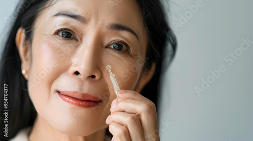 Closeup cut portrait of senior mature older Asian woman putting drop of antiaging pipette serum essence oil on finger hand. Anti wrinkle prevention skin care products concept. photo