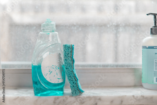 Close-up of a green sponge on a window sill next to a bottle of washing up liquid photo