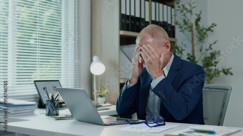 Businessman is seriously stressed and angry working on laptop and document paperwork and headache due to office syndrome on laptop and paperwork in the office.