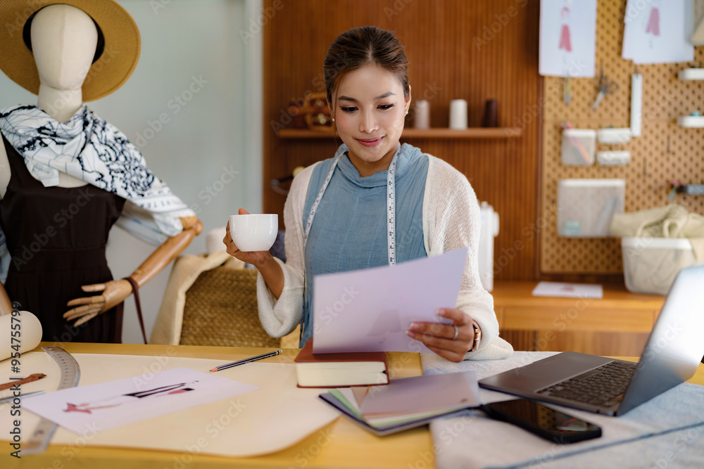 Fashion seamstress woman drinking coffee and checking sketch model of fashion clothes on paper Fashion seamstress woman drinking coffee and checking sketch model of fashion clothes on paper
