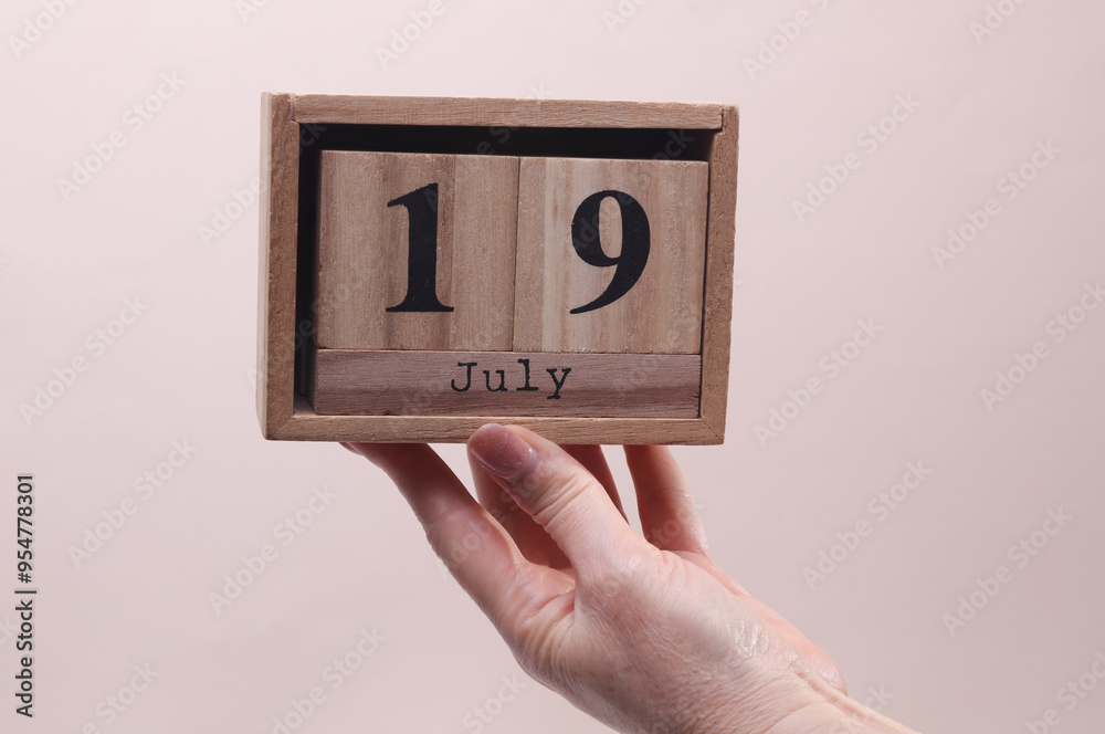 Female Hand holding wooden block calendar with the date July 19 on beige background Female Hand holding wooden block calendar with the date July 19 on beige background