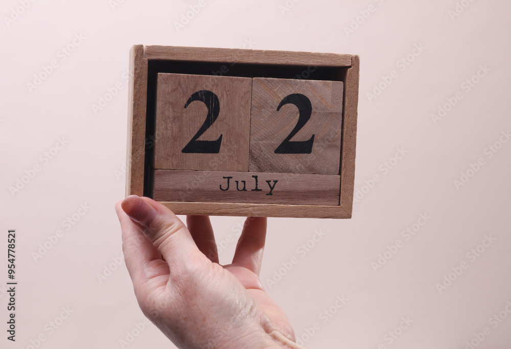 Female Hand holding wooden block calendar with the date July 22 on beige background Female Hand holding wooden block calendar with the date July 22 on beige background
