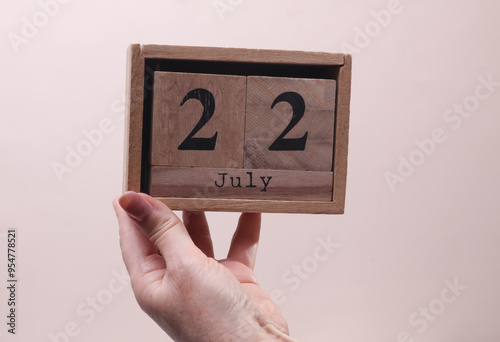 Wallpaper Mural Female Hand holding wooden block calendar with the date July 22 on beige background Torontodigital.ca