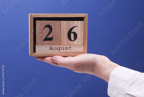 Wallpaper Mural Female Hand holding wooden block calendar with the date August 26 on a blue background Torontodigital.ca