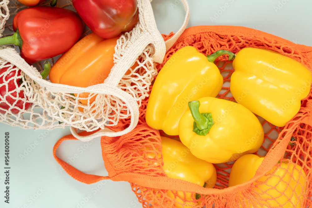 Φωτογραφία Red, orange, and yellow bell peppers in reusable mesh bags on light background, showcasing fresh, seasonal produce