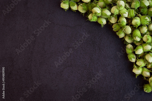 Fresh Green Hazelnuts on Dark Background. A close-up view of fresh green hazelnuts still in their husks, arranged in the upper corner of a dark, textured background. Top view. Copy space. photo