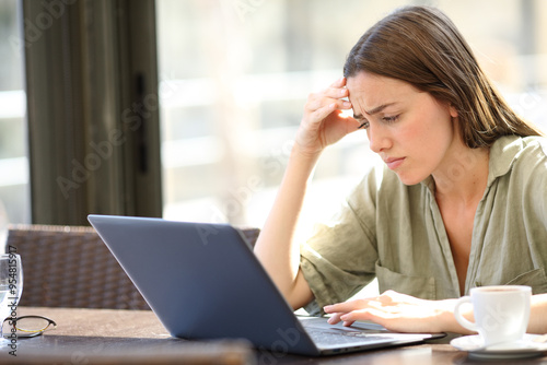 Worried woman in a bar checking bad news on laptop