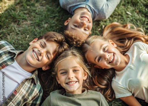 Happy children, two boys and two girls lie on the grass and look at the camera in the park on a summer day.Top view.