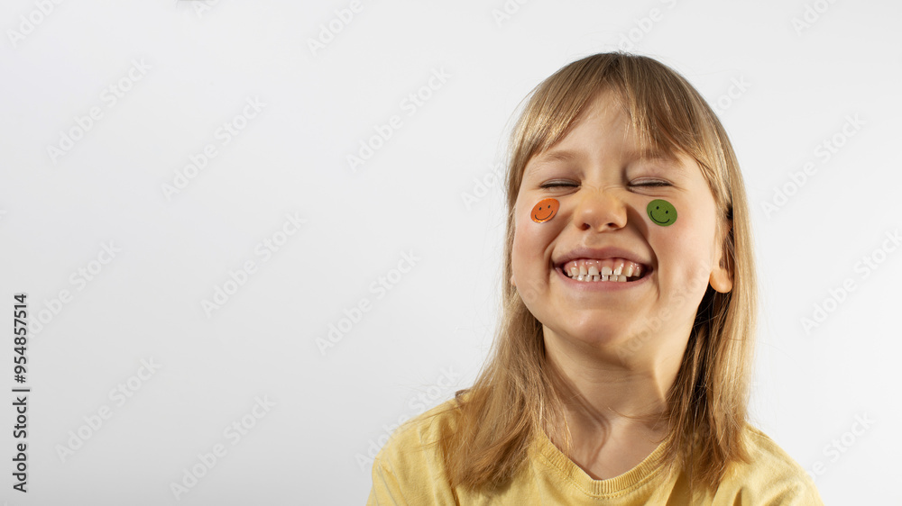 Little girl with emojis on cheeks smiles on light background. Copy space Little girl with emojis on cheeks smiles on light background. Copy space