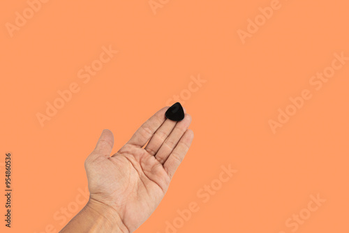 Black male hand holding a guitar pick isolated on orange background