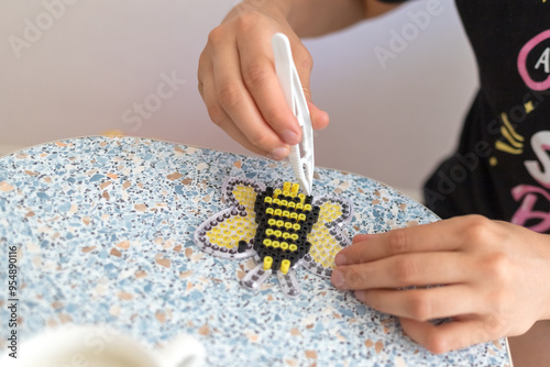 Girl is making toy. DIV concept. Plastic thermomosaic handmade. Modern hobby. Selective focus. Ironing beads photo