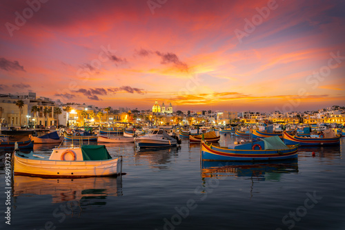 Sunset at Marsaxlokk, Malta picturesque fishing village, with colorful traditional boats reflecting in tranquil waters. photo