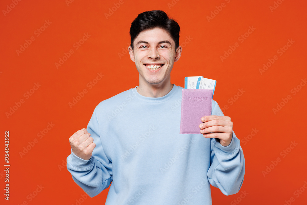 Traveler young man in blue casual clothes hold passport ticket do winner gesture isolated on plain red orange color background. Tourist travel abroad in free time rest getaway Air flight trip concept Traveler young man in blue casual clothes hold passport ticket do winner gesture isolated on plain red orange color background. Tourist travel abroad in free time rest getaway Air flight trip concept