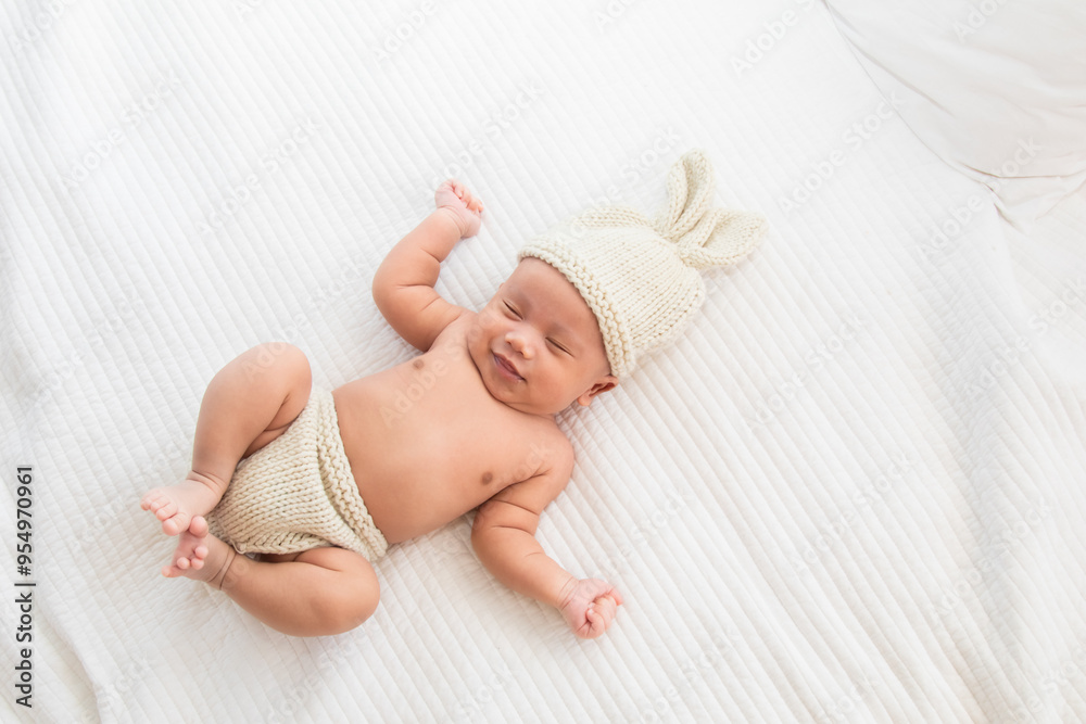 Asian adorable newborn baby wearing pants and rabbit hat beige knitted lying on white bed. little baby 0-1month play and talk with camera. Baby products concept. Happy childhood and motherhood