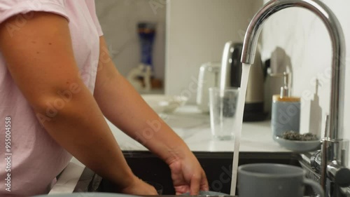 Detailed Close-Up of Dishwashing: Woman's Hands Washing Dirty Plates Under Running Water in Kitchen. High quality 4k footage
