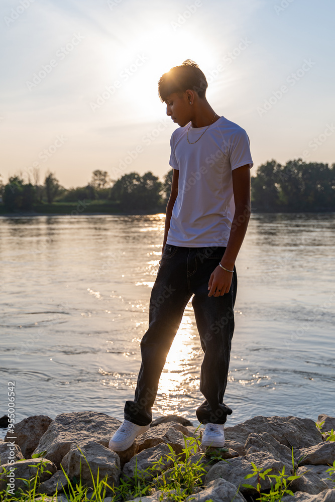 portrait of a young teenager standing on the river bank with the sun behind him portrait of a young teenager standing on the river bank with the sun behind him
