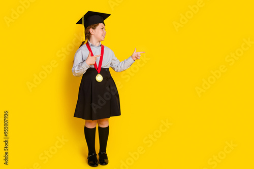 Full body portrait of little schoolkid mortarboard point fingers empty space girl wear uniform isolated on yellow color background