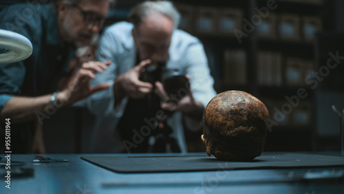 Two archaeologists talk and take photo of fossil remains of prehistoric human skull using professional camera on tripod. Scientists work in modern archaeological laboratory. Concept of archaeology. photo