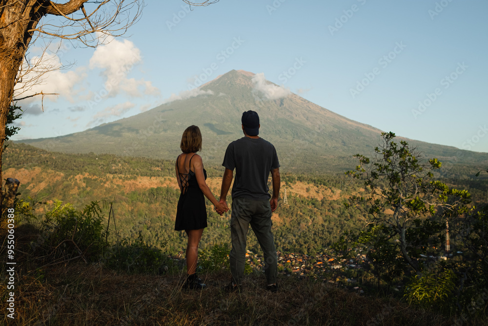 Fototapeta premium Couple Holding Hands with View of Mount Agung at Sunrise.
