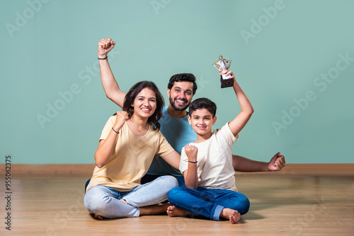 Indian boy or girl holding a trophy, celebrated by proud parents standing beside in a joyful moment photo