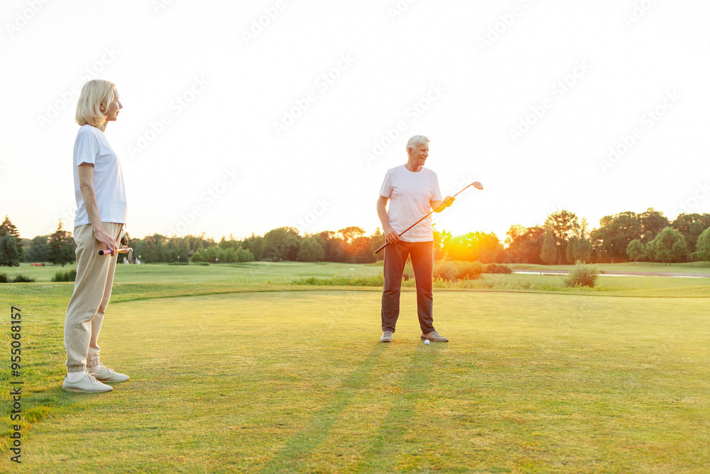 Obraz premium old senior couple in white clothes playing golf on golf course and chatting at sunset, elderly man and woman actively relaxing outdoors and laughing, pensioners on vacation