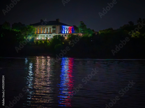 Embassy of France in Ottawa illuminated at night, colours of the tricolore (three-colour) flag, blue, white and red light reflecting on the Ottawa River, Ontario, Canada. Photo taken in August 2024. photo
