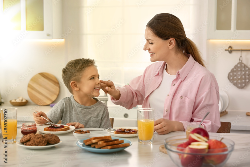 Mother and her cute little son having breakfast at table in kitchen on sunny morning Mother and her cute little son having breakfast at table in kitchen on sunny morning